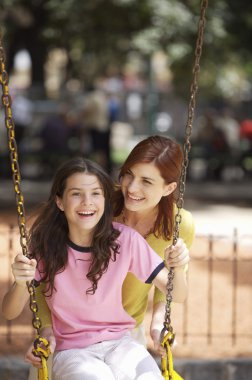 Mother and daughter playing on swing clipart