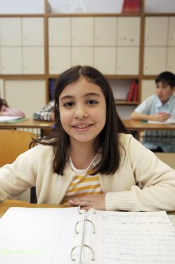 School girl sitting by the desk clipart