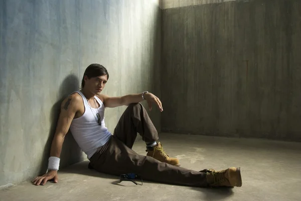 魅力的な若い男がコンクリートの床に座って壁にもたれて ストック写真
