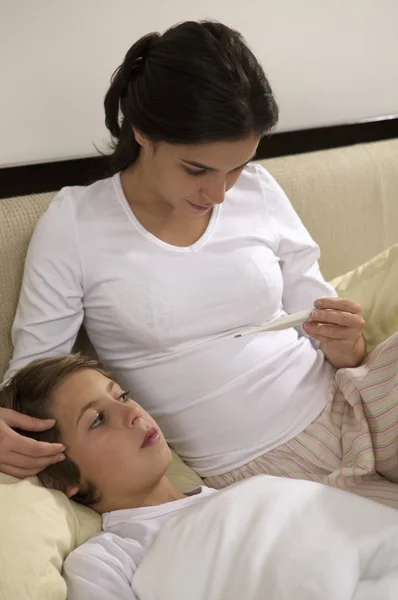 Mujer mirando termómetro y niño en la cama — Foto de Stock