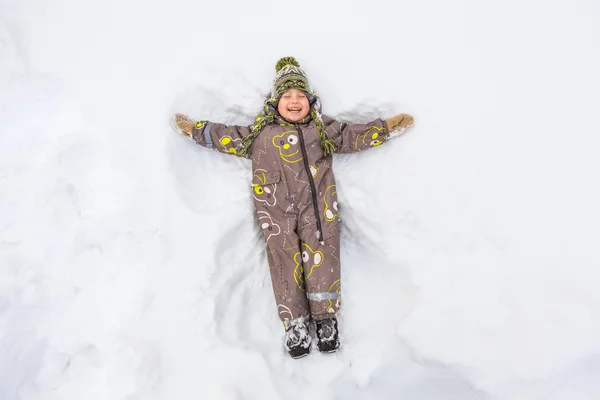 Мальчик лежит в снегу и смеется. Лицензионные Стоковые Фото