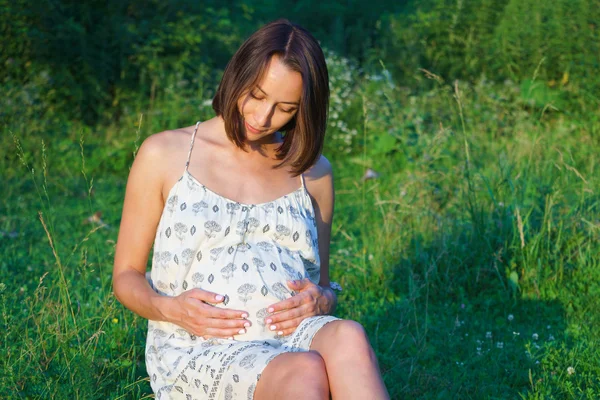 Pregnant girl sitting on the grass — Stock Photo, Image