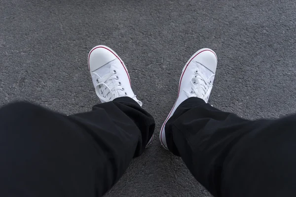Мужские ноги в черных брюках и белых кроссовках — стоковое фото