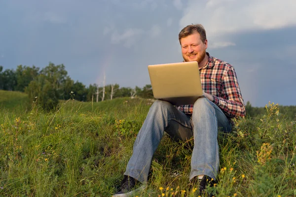Muž sedí na trávě s přenosným počítačem — Stock fotografie
