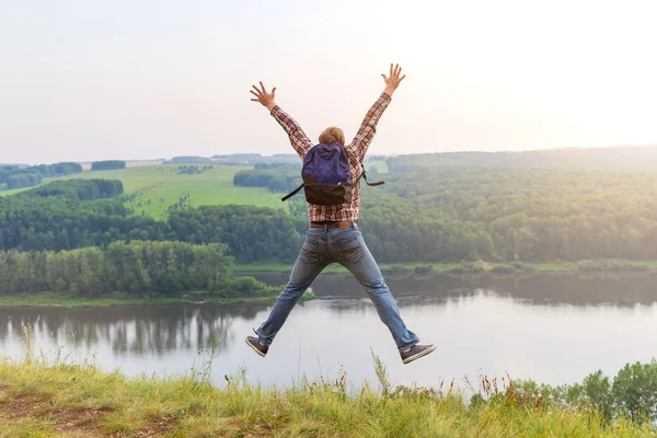 Man with a backpack jumping up on a hill. — Stock Photo, Image