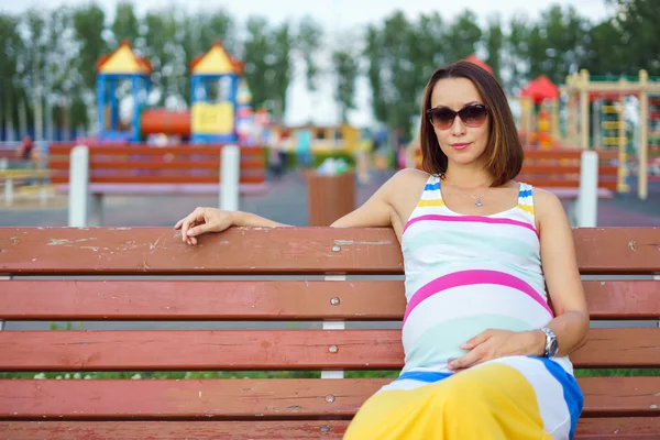 Schwangere sitzt auf Bank auf dem Spielplatz — Stockfoto