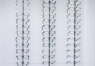 Glasses. Opticians shop. Glasses with diopters hang on  wall in several rows. clipart