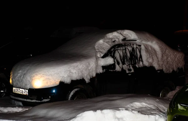 車は雪のドリフトで覆われヘッドライトをつけたまま夜は暗く路上に立っています 冬の天気 ロシアだ クラスノヤルスク 2021年1月30日 — ストック写真
