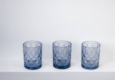 Beyaz zemin üzerinde zarif bir tasarım standı olan camdan yapılmış üç bardak. Kristal sofra takımı. Soyut siyah beyaz natürmort yaşam.