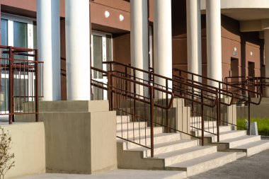 Merdivenleri olan ana giriş. Kahverengi duvarları ve beyaz sütunları olan apartman korkulukları. Yeni konut inşaatı.