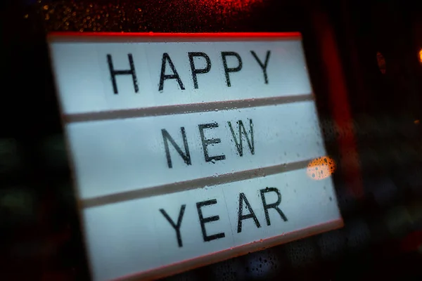 Lightbox Sign Happy New Year behind a glass door of the cafe during the rain at night.