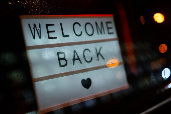 Lightbox dengan tanda WELCOME KEMBALI di belakang pintu kaca kafe selama hujan di malam hari. Kami buka lagi setelah karantina, foto pemilik usaha kecil. Stok Gambar Bebas Royalti