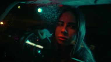 Güzel bir kadın düşünceli bir şekilde gece vakti yağmurun altında arabanın camından dışarı bakıyor..