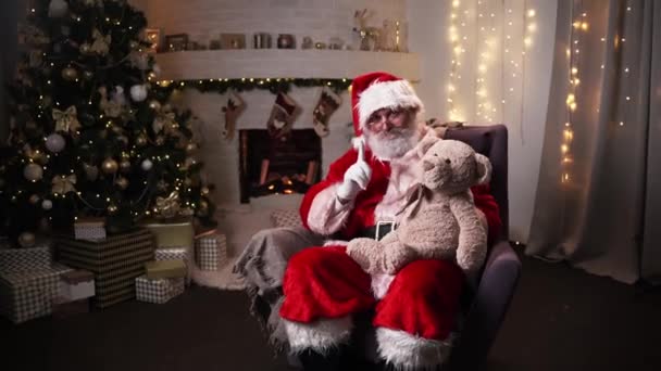 Legrační Santa Claus sedí v jeho rocker rok vánoční strom s medvídek vánoční duch, svátky a oslavy koncept 4k záběry — Stock video