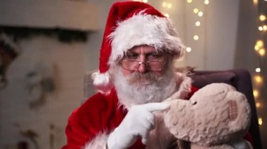 Komik Noel Baba, Noel ağacında Teddy Bear 'ın Noel ruhu, bayram ve kutlama konsepti 4K görüntüleriyle oturuyor.