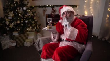Şöminenin yanında oturan komik Noel Baba maddesi ve Noel ağacı kum saatini çeviriyor - Noel ruhu, sihir, rüya konsepti 4k video