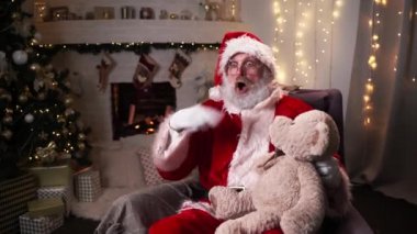 Komik Noel Baba, Noel ağacında Teddy Bear 'ın Noel ruhu, bayram ve kutlama konsepti 4K görüntüleriyle oturuyor.