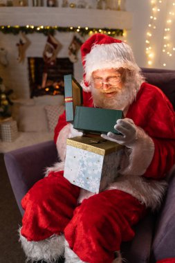 Noel Hediyeli Komik Noel Baba Kutusu. Yeni yıl hediyelerini seçiyorum. Noel Baba, Noel Ağacı Altında Sunar. Noel arifesinden önceki Aralık akşamı. Yeni yıl Noel Ruhu kavramını kabul et.