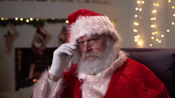 クリスマスツリーの近くに彼のロッキングチェアに座って、眼鏡で怒っているサンタクロースの肖像画。4K解像度でクリスマス、休日やお祝いの概念 — ストック動画