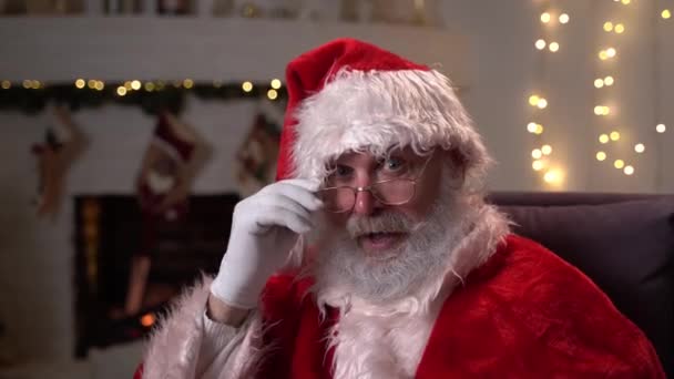 Портрет счастливого смешного Санта-Клауса в очках, сидящего в кресле-качалке возле елки. Концепция Рождества, праздников и торжеств с разрешением 4K — стоковое видео
