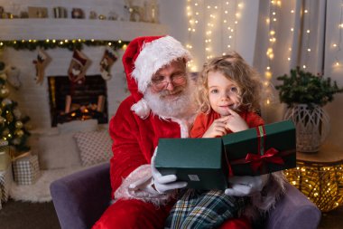 Komik Noel Baba sallanan sandalyesinde dizinde tatlı bir çocukla oturuyor ve özel bir hediyeyi birlikte açıyor. Noel ruhu, tatiller ve kutlama konsepti