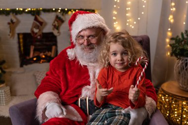 Komik Noel Baba sallanan koltuğunda dizinde Noel Lolipopu olan sevimli bir çocukla oturuyor. Noel ruhu, tatiller ve kutlama konsepti