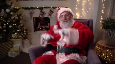 Noel ağacının yanındaki dekore edilmiş dairede taşak ve çakmakla dans eden komik Noel Baba portresi. Kutlamalar ve neşeli insanlar konsepti.