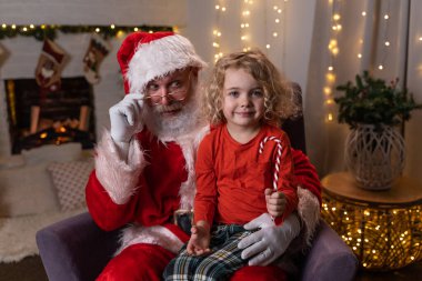 Komik Noel Baba sallanan koltuğunda dizinde Noel Lolipopu olan sevimli bir çocukla oturuyor. Noel ruhu, tatiller ve kutlama konsepti