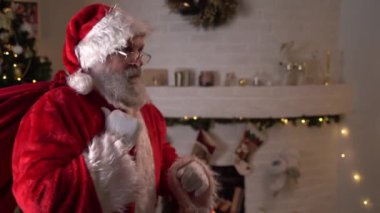 Bir çanta dolusu hediyeyle Noel Baba gidip kameraya bakar ve şşşş der. Evin arka planı, Noel dekoru ve Noel ağacı. Noel 'den Önce Aralık Akşamı Yeni Yıl Rüya Kavramı