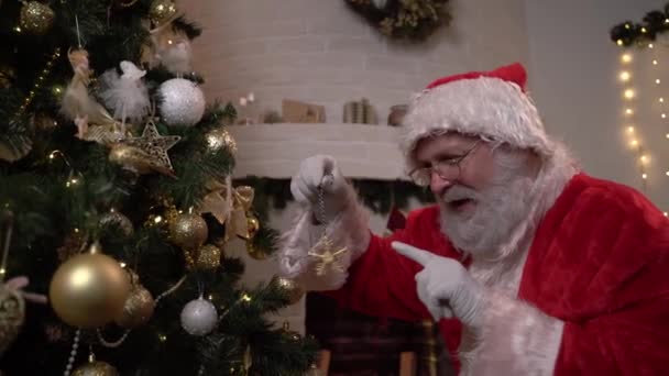 Papai Noel pendura uma estrela de brinquedo de árvore de Natal na árvore de Natal. Conceito do espírito de Natal, feriados e celebrações — Vídeo de Stock