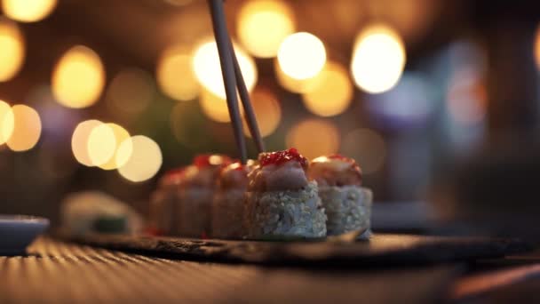 Palos Tome sushi en el fondo de las luces del restaurante. Variedad de tipos de sushi con caviar rojo, pescado, queso Filadelfia y palillos de cerca. Conjunto de deliciosos rollos de sushi japonés en una tabla de piedra — Vídeos de Stock
