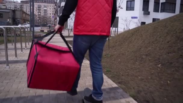 Vista trasera de monopatín mensajero masculino con comida mochila a caballo en la calle. Hombre de uniforme rojo entregando orden. Concepto de servicio de reparto de alimentos. — Vídeos de Stock