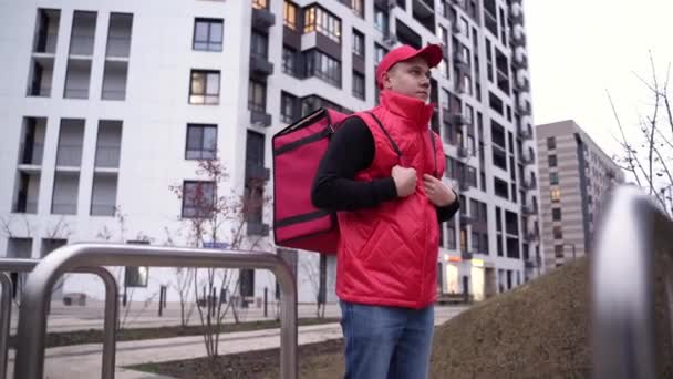 Portret doręczyciela w czerwonym mundurze z torbą termiczną w tle nowoczesnych budynków. Koncepcja dostaw żywności — Wideo stockowe