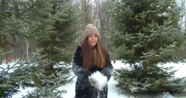 Oyuncu genç kadın ormandaki ağacın önüne kar atıyor ve gülümsüyor. İlk Kar ve Kış Konsepti