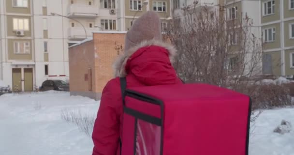Suivez la photo de la femme de livraison portant un uniforme rouge smartphone tout en marchant le long des bâtiments dans la rue de la ville avec un sac isolé — Video