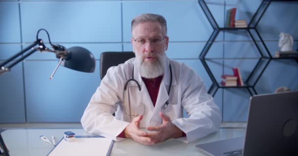 Médecin professionnel avec barbe en uniforme médical blanc parlant à la caméra faire un chat vidéo conférence téléphonique ou enregistrement de la formation webinaire de soins de santé parler à un patient éloigné — Video
