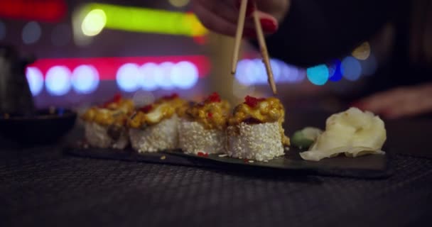 Žena si bere sushi tyčinky v tradiční japonské restauraci s výhledem na noční město. Tyčinky Take Sushi v restauraci světla pozadí. Sada lahodných japonských sushi rohlíků na kamenné desce — Stock video