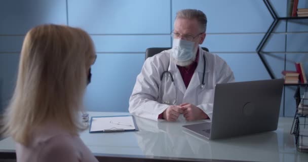 Examen médico primario. Médico en máscara protectora dando paciente femenino en el termómetro. Control de pacientes en consultorio médico. — Vídeo de stock