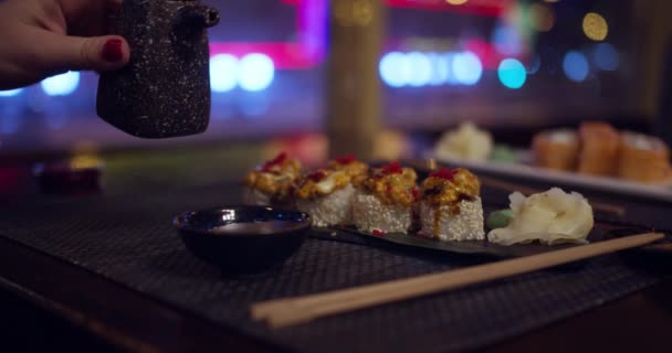 Soya sosunu soslu sandığa döker. Gece şehri manzaralı. Suşi malzemeleri. Japon restoranındaki küçük tabağa soya sosu dökerek. Dökülen kahverengi sıvıyı kapat. — Stok video