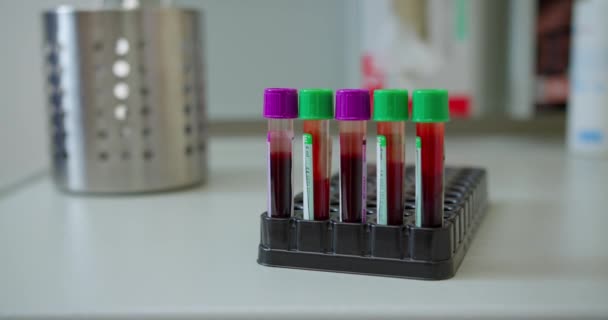 Uma mão enluvada de enfermeiras tira amostras de sangue. Tubos de teste com amostras de sangue para coronavírus em um rack em um laboratório ou hospital. Exames laboratoriais de sangue de pacientes para COVID-19. O conceito de — Vídeo de Stock