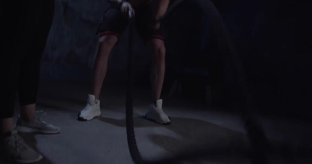Coach visar en fitness kvinna hur man gör en övning med ett rep. Stark man tränar i cross training gym gjorda inuti gamla gym. — Stockvideo