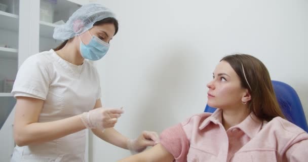 安全手袋と保護マスクの医療看護師は、保健クリニックの女性患者にワクチン注射を行っています。医者は治療として薬のショットを置くために低血圧針と注射器を使用します — ストック動画