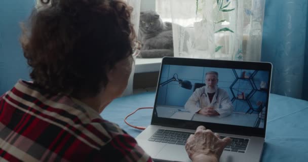 Berufskraftmediziner mit Bart in weißer medizinischer Uniform Videokonferenzen mit einer Patientin aus der Ferne, die während einer telemedizinischen Videotelefonie in einer Konferenz über die Pandemie des Coronavirus berät — Stockvideo