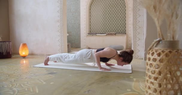 Sporty Curly-Haired Woman Does Yoga Stretching Exercises. Slender girl does yoga In a bright, atmospheric yoga room in the morning — Stock Video