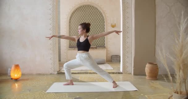 Sporty Curly-Haired Woman Does Yoga Stretching Exercises. Slender girl does yoga In a bright, atmospheric yoga room in the morning — Stock Video