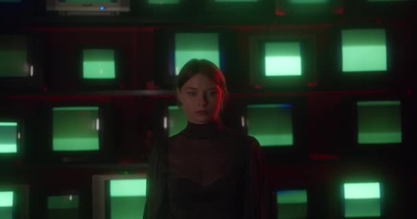 Junges Mädchen blickt vor dem Hintergrund alter Fernseher mit statischem und grünem Bildschirm in die Kamera — Stockvideo
