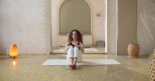 Sporty Curly-Haired Woman Does Yoga Stretching Exercícios. Menina esbelta faz ioga Em uma sala de ioga brilhante e atmosférica pela manhã — Vídeo de Stock