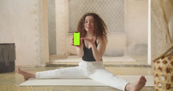 Curly-Haired kvinna fitness coach visar övningar online med hjälp av smartphone med grön skärm. Online lärande och studier, aktiv hälsosam livsstil sportig kvinnlig träning hälsa och inomhus — Stockvideo