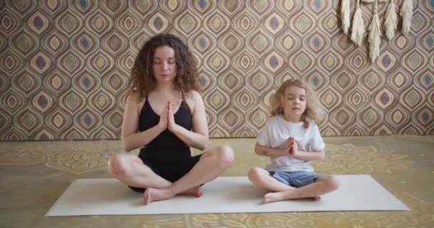 Moderne glad sund familie barn søn og ung mor har det sjovt at lave yoga øvelser sammen sidde i lotus udgør, smilende opmærksomme mor undervise lille søde barn dreng til at meditere på yoga studie – Stock-video