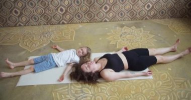 Modern mutlu, sağlıklı aile çocuğu oğul ve genç anne birlikte yoga egzersizleri yaparak eğleniyorlar. Lotus pozunda oturup gülümseyen anne, küçük tatlı çocuğa yoga stüdyosunda meditasyon yapmayı öğretiyor.